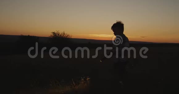 一个可爱的男孩在日落时用手电筒穿过草地视频的预览图