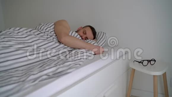 大胡子男人躺在毯子下面的床上醒来微笑着戴上眼镜咂嘴视频的预览图