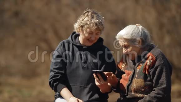 一位妇女在她年迈的母亲的智能手机上展示照片一位妇女帮助她年迈的母亲使用她的智能手机视频的预览图