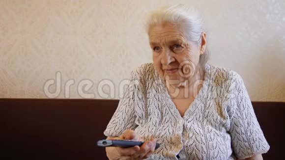 老妇人用遥控器和微笑切换电视频道奶奶在看电视视频的预览图