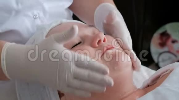 美容术中闭眼清洁女孩颈部脸颊和前额皮肤的方法视频的预览图