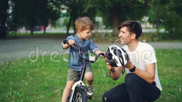 动作缓慢的年轻人小心的父亲拿着自行车头盔和儿子谈论安全然后戴上头盔视频的预览图