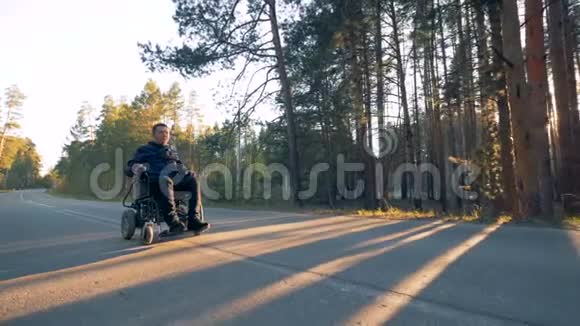 在森林里一个身材矮小的人正坐着他的电动轮椅沿着道路前进视频的预览图