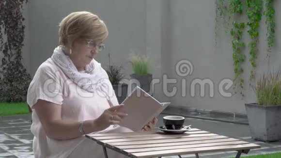 一位漂亮的老妇人正坐在露台上看书视频的预览图