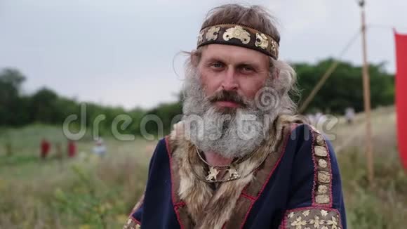 一位身穿民族服装留着大白胡子的老人站在田野里看上去又伤心又疲惫视频的预览图