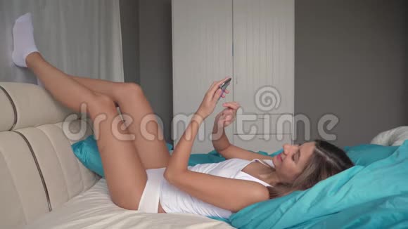 女人躺在床上双腿仰躺在床上使用智能手机视频的预览图