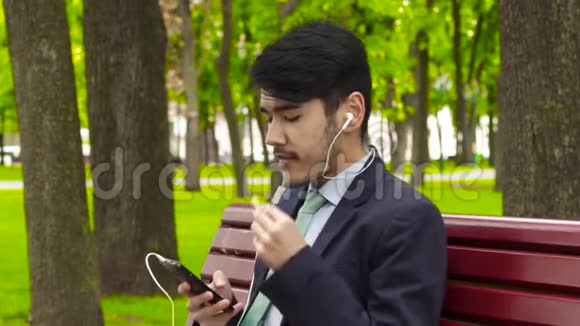 亚洲商人坐在公园里用耳机吃炸薯条视频的预览图