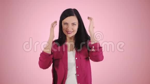 精力充沛的女孩在粉红背景的工作室她穿着五颜六色的衬衫尾巴上的黑发在移动慢慢视频的预览图