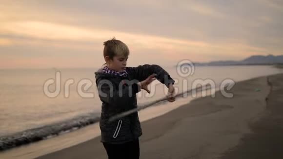 那个男孩在日落时站在海滩上把手里的棍子转过来视频的预览图