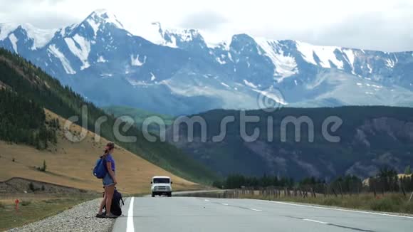 年轻的旅游妇女带着背包穿着短裤在山路上搭便车下雪了视频的预览图