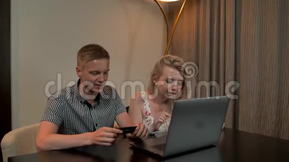 漂亮的男人和女孩坐在沙发上在笔记本电脑上用信用卡在线购物视频的预览图