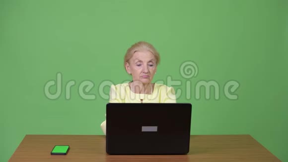 漂亮的高级女商人用手机和笔记本电脑视频的预览图