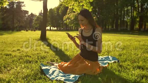 年轻的女士享受自然和日落使用手机坐在绿色夏季公园视频的预览图