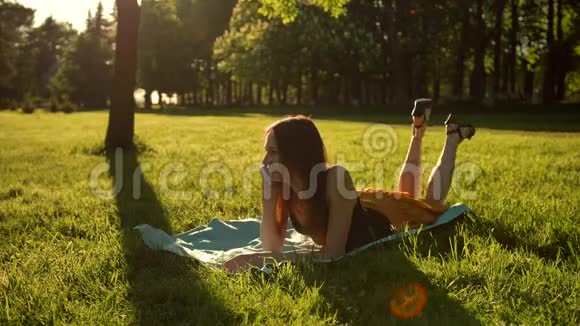 漂亮的女孩躺在草地上用智能手机说话女性从腹部到背部翻转视频的预览图