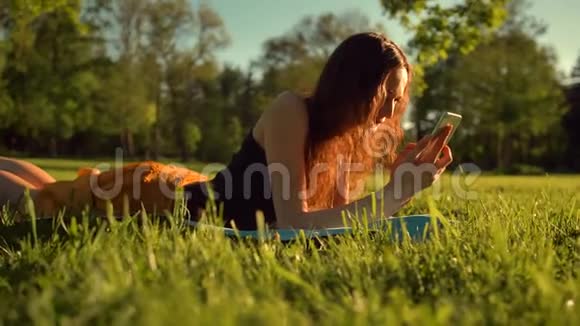 快乐女孩打字短信躺在公园的草地上女人在电话里聊天视频的预览图