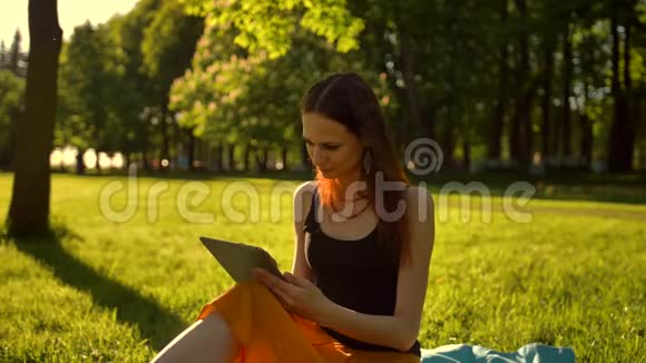 年轻的女士在绿草上浏览她的平板电脑视频的预览图