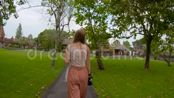 一名年轻女子在巴厘岛的皇家宫殿塔曼阿云TamanAyun散步时被UHD慢镜头拍摄视频的预览图