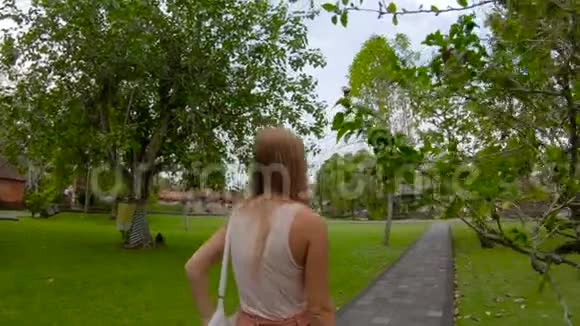 一名年轻女子在巴厘岛的皇家宫殿塔曼阿云TamanAyun散步时被UHD慢镜头拍摄视频的预览图
