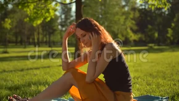 快乐迷人的女士坐在绿草上通过数字电话交谈视频的预览图