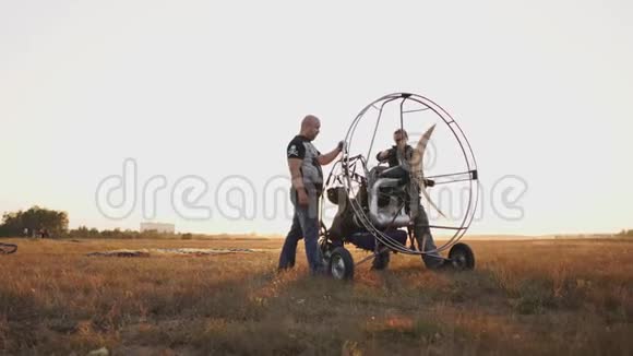 汽车滑翔伞在日落时用一个木制螺旋桨站在一片田野里两名飞行员在飞行前热身发动机A视频的预览图