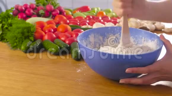 女人的手用蓝色碗里的木抹刀在桌子上用蔬菜揉酵母面团侧视图视频的预览图
