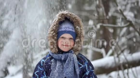 冬天森林里一个美丽的金发小男孩的肖像下雪了视频的预览图