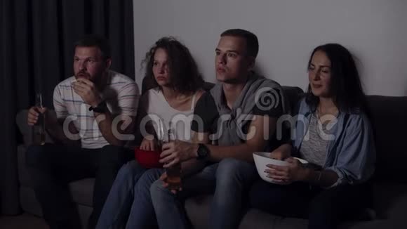 四个朋友一起吃爆米花喝啤酒一起看恐怖电影非常着迷和害怕坐着不动视频的预览图