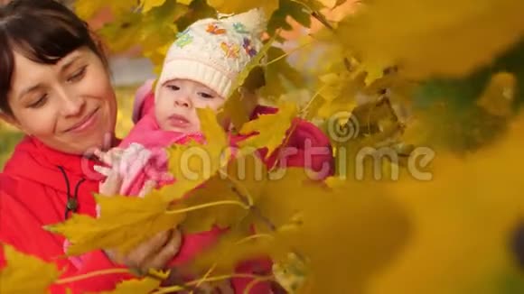 宝宝和妈妈微笑着抚摸公园里黄色的秋叶慢动作视频的预览图
