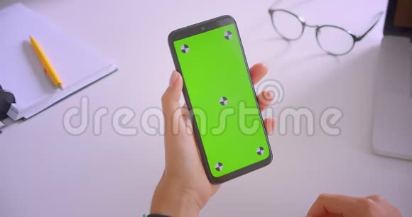 室内办公桌上使用带有绿色彩色键屏手机的白人女商人手的特写照片视频的预览图