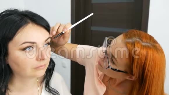红发造型师化妆师在美容院做时尚的黑色长发模特晚妆视频的预览图