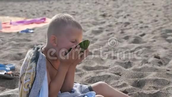 孩子们在海滩上玩在沙子里吃西瓜的男孩这孩子手里拿着一块绿色的瓜皮头视频的预览图