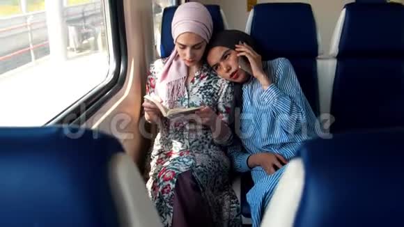 两个坐火车旅行的穆斯林妇女一个在看书另一个在打电话视频的预览图