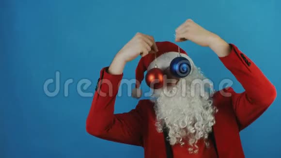 新年男人就像一个圣诞老人带着蓝色背景的红色和蓝色圣诞球玩具视频的预览图