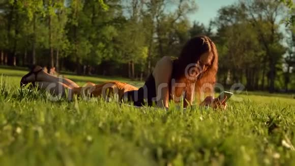 快乐女人打短信或聊天坐在公园的草地上女人在电话里聊天视频的预览图