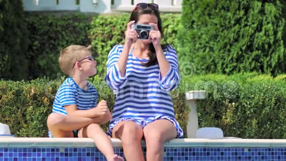 母亲和儿子坐在游泳池的边缘用一台照相机拍摄大自然的照片视频的预览图