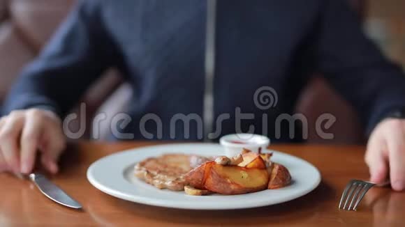 一个年轻人在咖啡馆里吃了一份开胃的牛排里面有土豆和酱汁视频的预览图