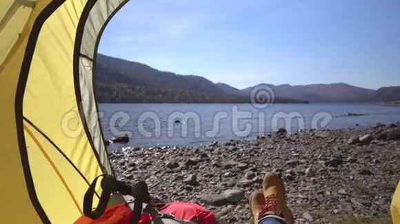 女旅行者躺在山湖畔的一个黄色帐篷里然后女旅行者来到了湖的海岸视频的预览图