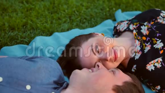 快乐的年轻夫妇躺在日出的草地上泰尔和橙色视频的预览图