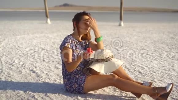 快乐的微笑女孩享受日落吃西瓜坐在盐上柱子上视频的预览图