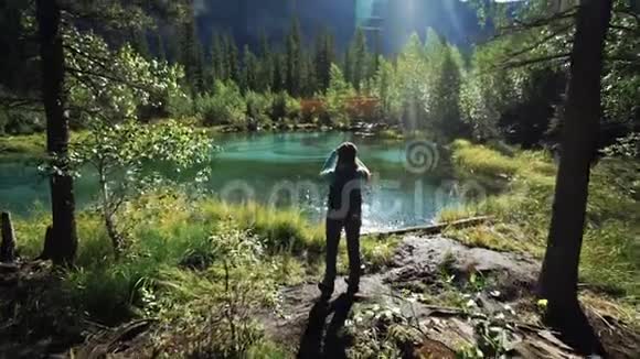 一位年轻的女游客正站在一个美丽的蓝色湖泊上在阳光明媚的日子里为风景优美的风景拍照视频的预览图