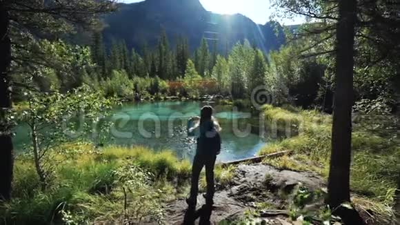 一位年轻的女游客正站在一个美丽的蓝色湖泊上在阳光明媚的日子里为风景优美的风景拍照视频的预览图