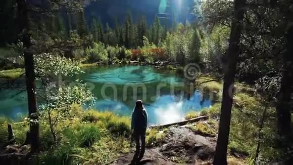阳光明媚的一天年轻的女游客站在山上一个风景如画的蓝色湖泊上长镜头后景视频的预览图
