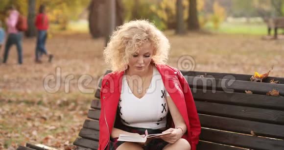 日落时分漂亮的年轻女人在户外的长凳上看书视频的预览图