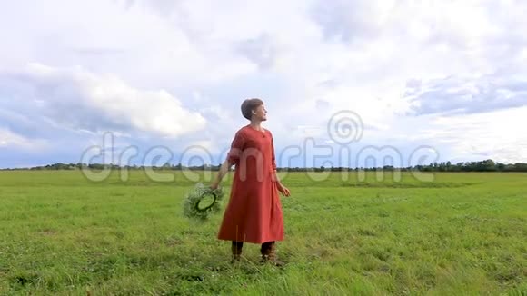 一位身着民族服装的妇女在暴风雨天的背景下拿着花圈在纺纱慢动作视频的预览图
