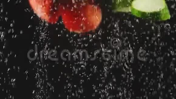 黄瓜和番茄片溅在水中的黑色背景有气泡的水中新鲜蔬菜视频的预览图