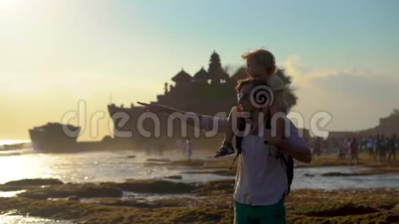 日落时分一对父子在巴厘岛美丽的塔纳罗特神庙的海岸线上散步视频的预览图