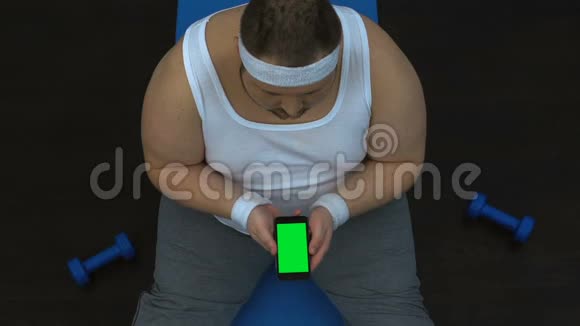 胖子运动装看智能手机健身指南练习体育博客视频的预览图