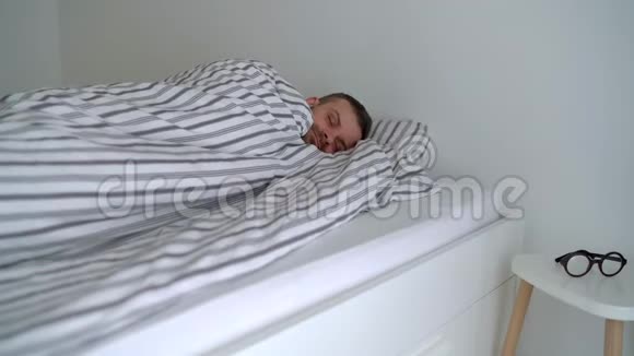 大胡子男人躺在毯子下面的床上醒来微笑着戴上眼镜咂嘴视频的预览图