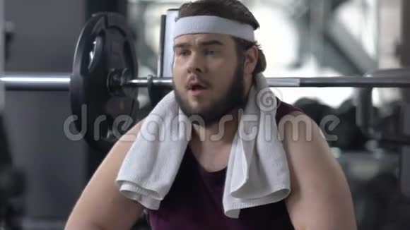 有趣的肥胖男子对运动员们在健身房训练缺乏安全感而羡慕不已视频的预览图