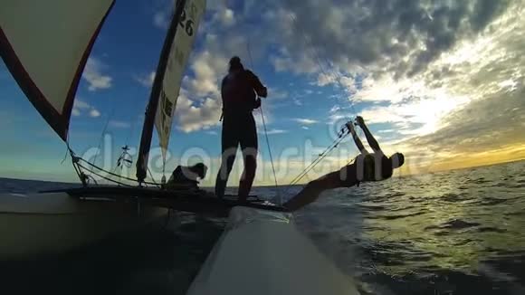 三个人在海面上的暮色中航行在帆板双体船上视频的预览图